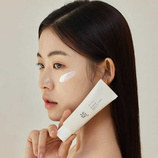 Mujer asiática aplicando protector solar Beauty of Joseon Relief Sun con tubo en la mano y crema en la mejilla