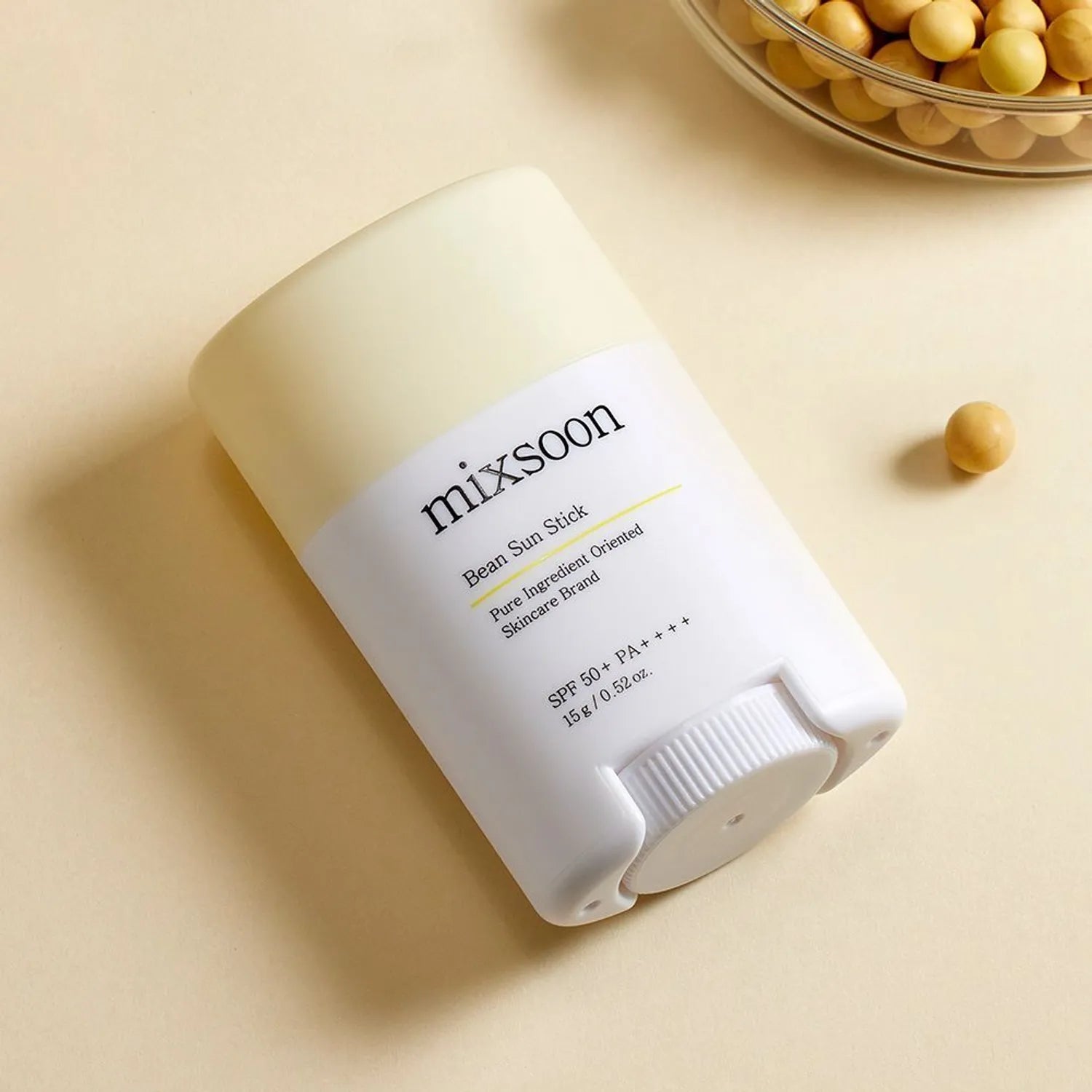 Barra de protector solar mixsoon Bean Sun Stick sobre superficie beige con frijoles a un lado